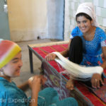 Teamwork. The girl on the right holding a hank of silk thread assists the other girl winding a ball.