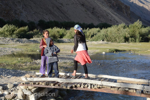 Kids are crossing a crude bridge over the side creek.