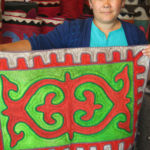 Dinara, the manager of the Altyn Kol handicraft shop, a women’s co-operative, proudly displays a Shirdak (felt carpet) with a traditional design.