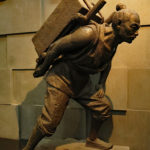 Bronze statues showing how men carried and shaped the stones for the wall.