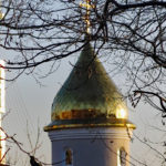 A golden onion tower of a Russian Orthodox church glows in the afternoon light.