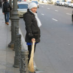 A lady picked up trash on a sidewalk using the typical Russian broom.